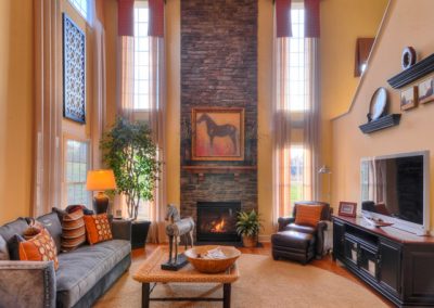 two story room with stone fireplace and ceiling beams